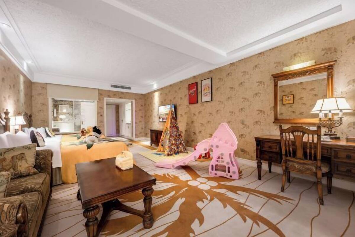 A hotel room with a bed, a wooden table, a chair, a desk, a lamp, and a decorative horse figure.