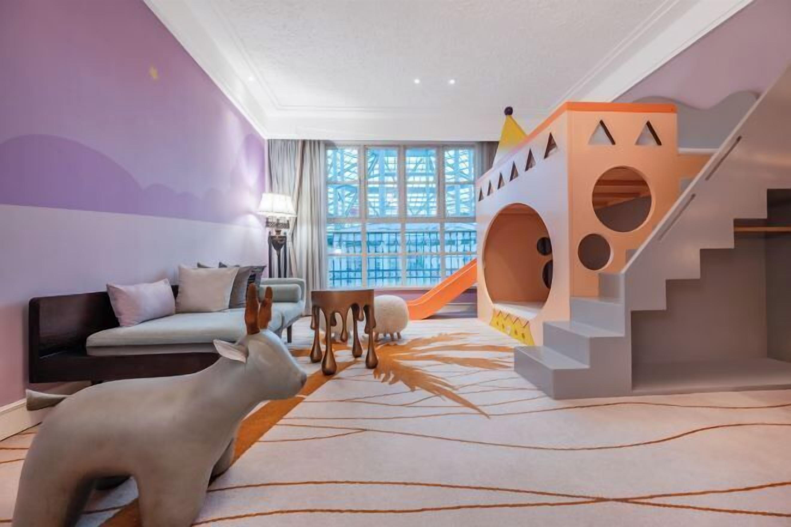 Espaço infantil com escorrega, estrutura de escalada e um sofá numa sala com carpete estampado.