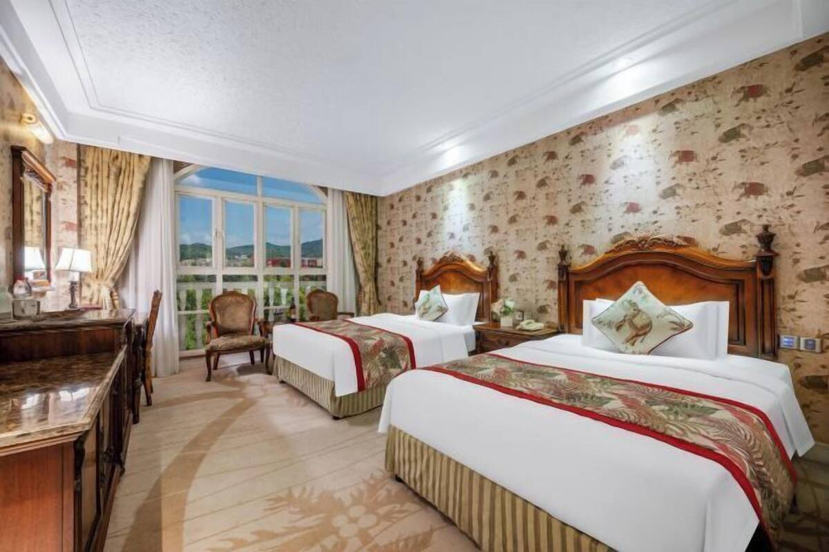A hotel room with two beds, a desk, a chair, and a large window with a view.