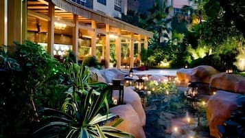 Un patio de hotel con fuente, zonas de estar y un edificio de varios pisos con grandes ventanales.