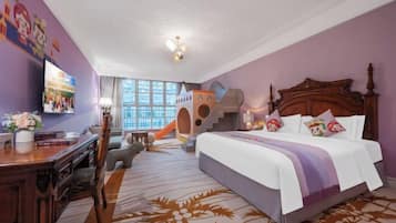A hotel room with a large bed, a desk, a chair, a TV, and a play area with a slide.