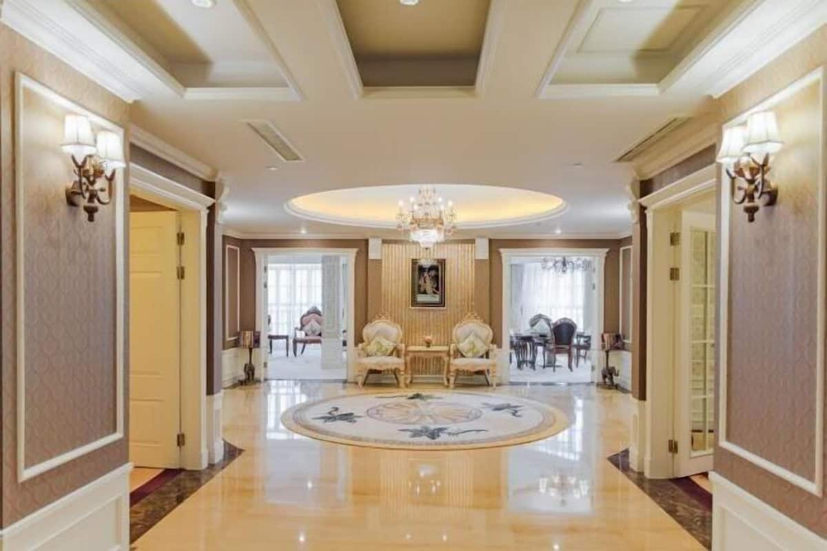A grand hallway with a chandelier, a round table, and two chairs.