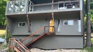 Eine zweistöckige Holzhütte mit einer Holztreppe, einem Balkon und einer kleinen Veranda.