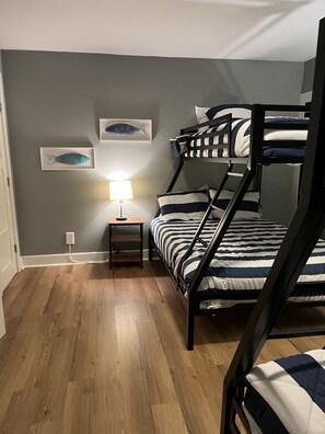 Una camera con un letto a castello, pavimento in legno, un comodino con lampada e due quadri con pesci appesi al muro.