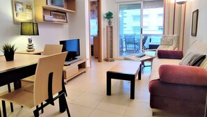 Een moderne woonkamer met een televisie, eettafel, stoelen, een bank en een glazen schuifdeur naar een balkon.