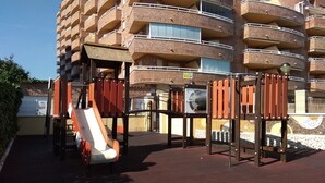 A playground with a slide and climbing structures in front of a multi-story building with balconies.