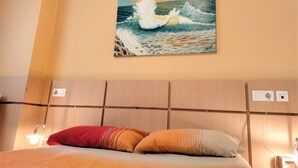 Une chambre d’hôtel avec un lit, un tableau représentant une vague et une tête de lit en bois.