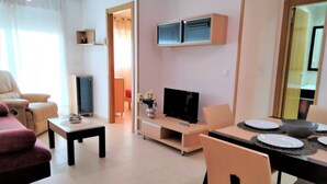 Un salon moderne avec un canapé, un téléviseur et un coin repas avec une table mise pour deux personnes.