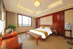 Quarto de hotel com uma cama grande, um banco de madeira, uma escrivaninha, um vaso e vista para a cidade.