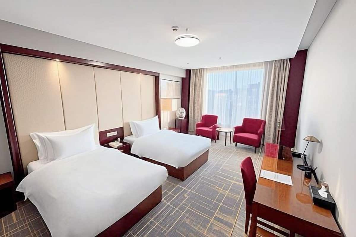 Hotellihuone, jossa on kaksi sänkyä, työpöytä, tuoli ja pieni pöytä.