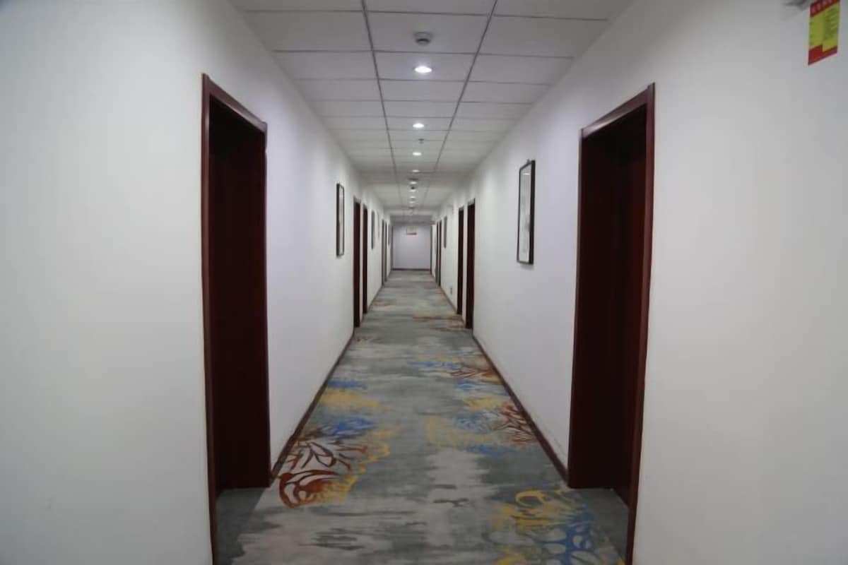 Um corredor longo com carpete estampado, paredes brancas e portas de madeira.