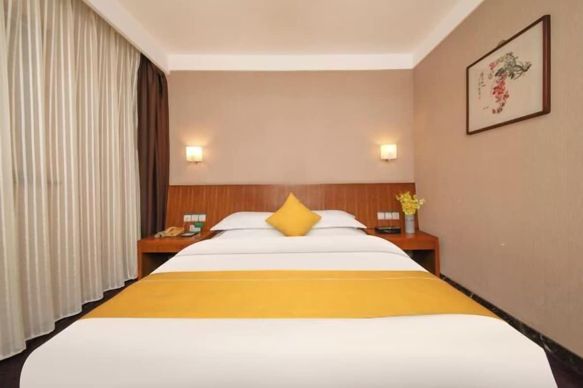 Quarto de hotel com uma cama grande, duas mesas de cabeceira, um criado-mudo, um telefone fixado na parede e uma obra de arte emoldurada.