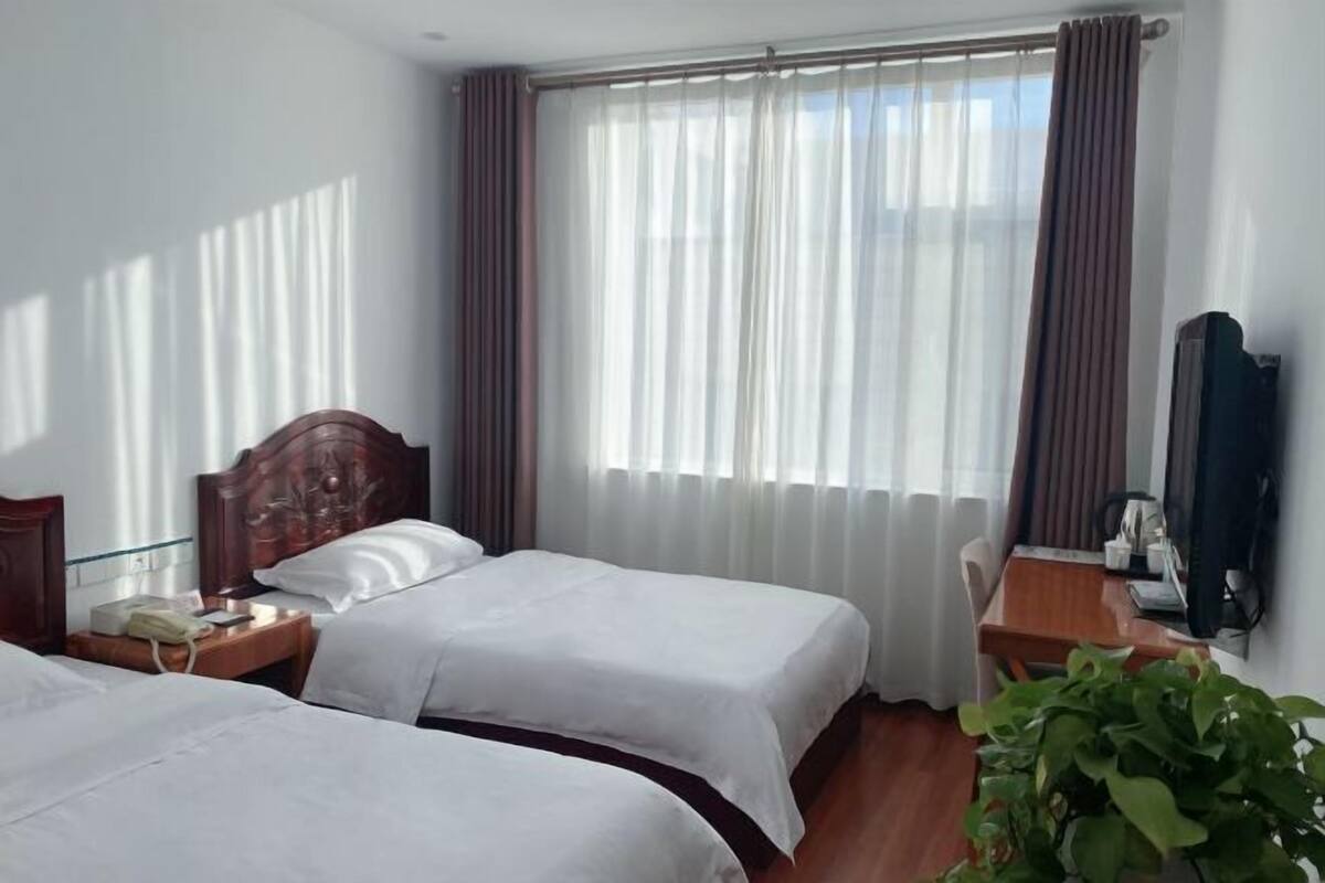 Hotellihuone, jossa on kaksi sänkyä, puinen sängynpääty, työpöytä tuolilla, puhelin ja televisio.