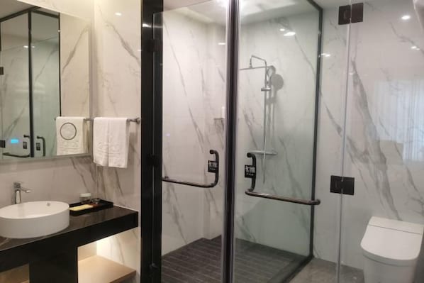 Een moderne badkamer met een douchecabine van glas, een rond wastafeltje en een toilet.