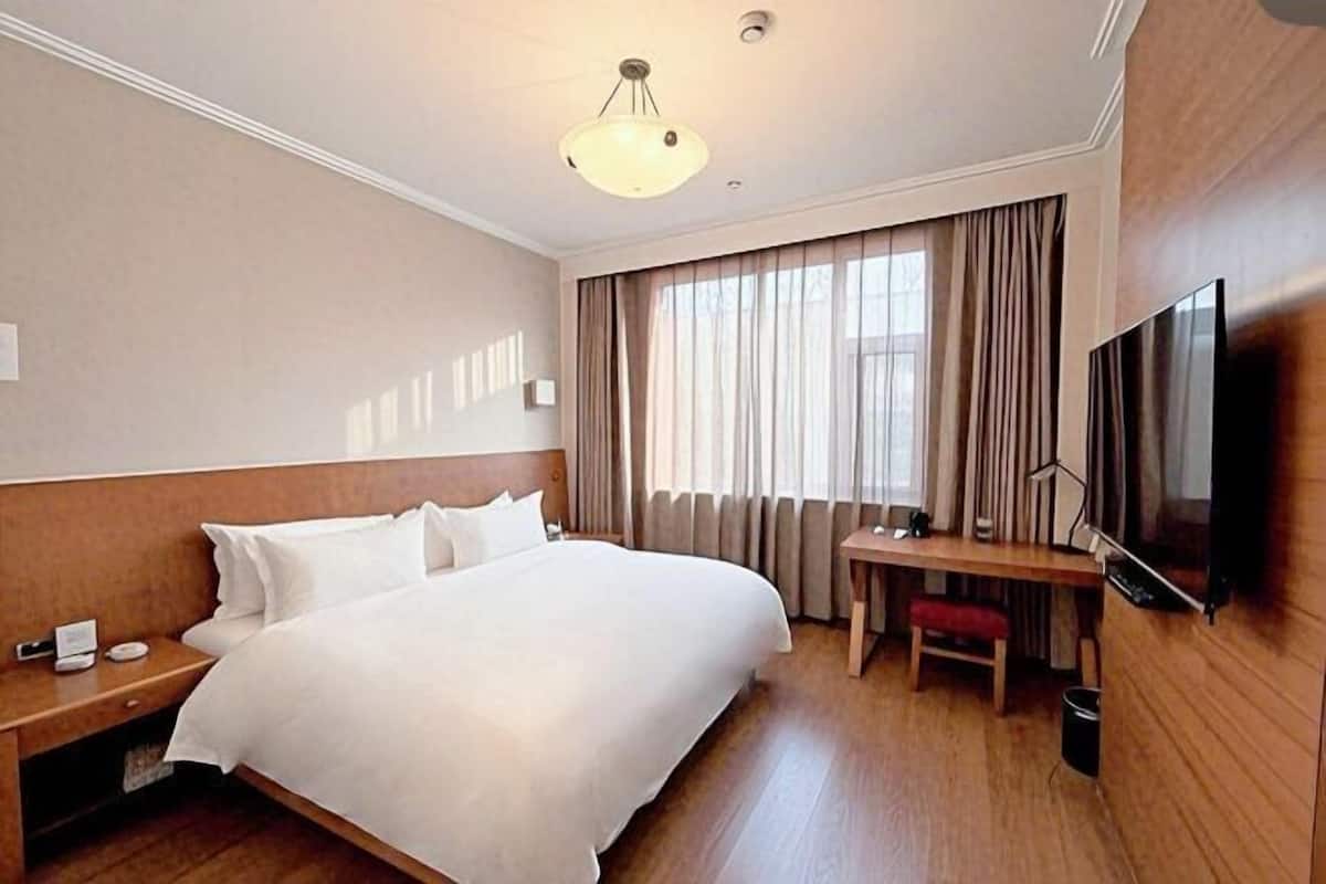 Hotellihuone, jossa on suuri sänky, työpöytä, televisio ja ikkuna, jossa on verhot.