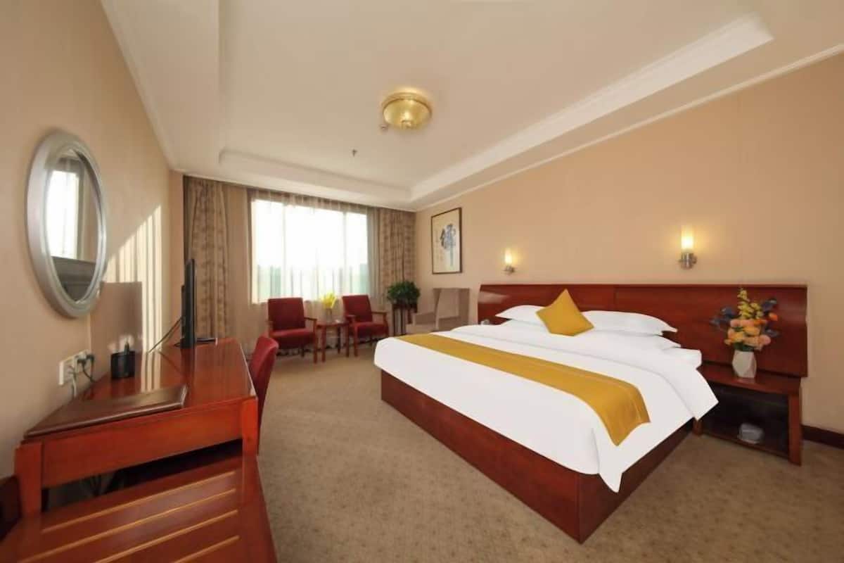 Hotellihuone, jossa on suuri sänky, työpöytä, tuoli ja pieni pöytä.
