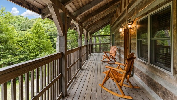 A wooden porch with rocking chairs and a view of a forest.