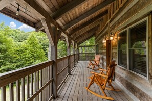 A wooden porch with rocking chairs and a view of a forest.