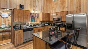 A spacious kitchen with wooden cabinets, a stainless steel refrigerator, and a granite countertop.