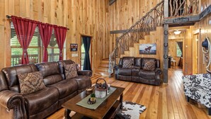 A spacious cabin interior with two leather sofas, a wooden staircase, and a 'Welcome' sign.