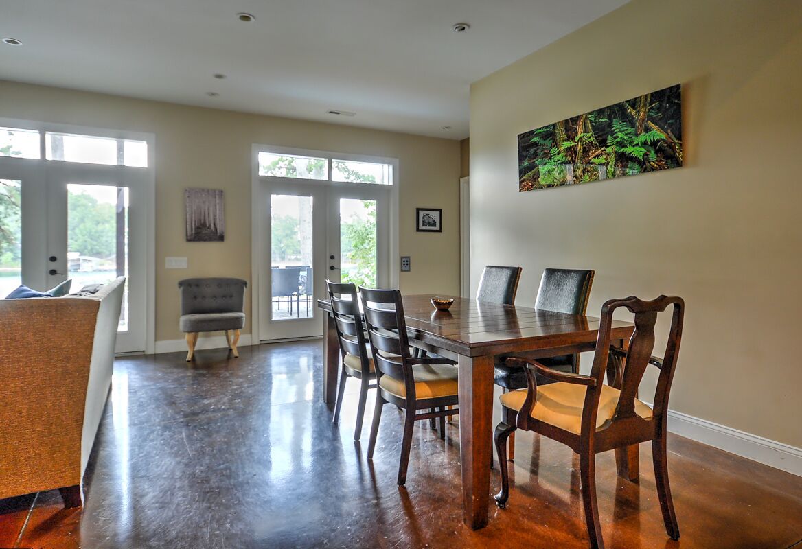 A dining area with a wooden table and chairs, a gray armchair, and a painting on the wall.