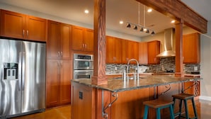 Una cocina con armarios de madera, electrodomésticos de acero inoxidable, encimera de granito y taburetes de bar.
