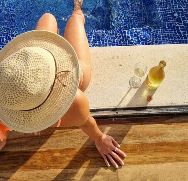 A person relaxing by a poolside with a straw hat, a glass of white wine, and a bottle of wine. - Hacienda Arenal Luxury Village (Peñas Blancas)