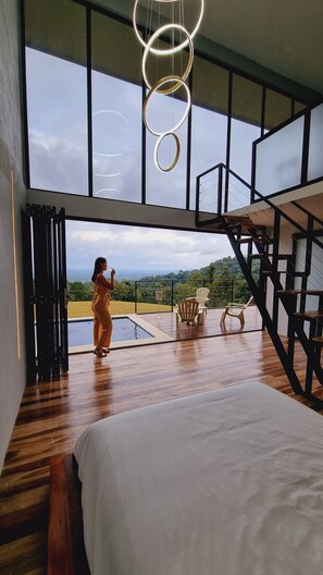 Quarto espaçoso com uma cama grande, piso de madeira e vista para o exterior por grandes janelas.