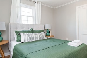 A neatly arranged bedroom with a bed, two bedside tables, a window with curtains, and a door.