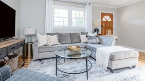 A modern living room with a grey sectional sofa, a glass coffee table, and a white ottoman.