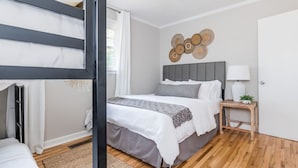 A modern bedroom with a bunk bed, a grey upholstered headboard, a bedside table with a lamp, and a decorative wall piece.