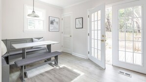 A bright, white interior with a bench and table, large windows, and a door leading outside.