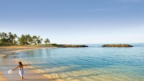 Une scène de plage avec une eau claire, une personne qui se promène le long du rivage et des palmiers en arrière-plan.