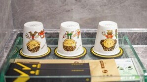 Three white mugs with cartoon characters and gold trim on a glass tray.