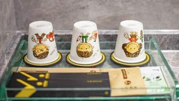 Drie witte mokken met tekenfilmfiguren en gouden rand op een glazen dienblad.
