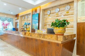 A reception desk with a wooden counter, clocks, a laptop, and a potted plant.