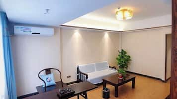 Una sala de estar con un sofá, una mesa de centro, una silla, una mesita con una planta y un aire acondicionado.