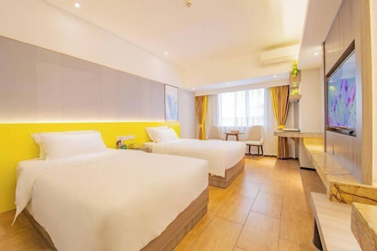 A hotel room with two beds, a desk, a chair, and a TV.