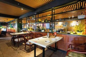 Een restaurantinterieur met houten plafondpanelen, een bar met planken en eettafels met stoelen.