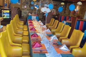A long dining table with yellow chairs, set with red and white napkins, and balloons.