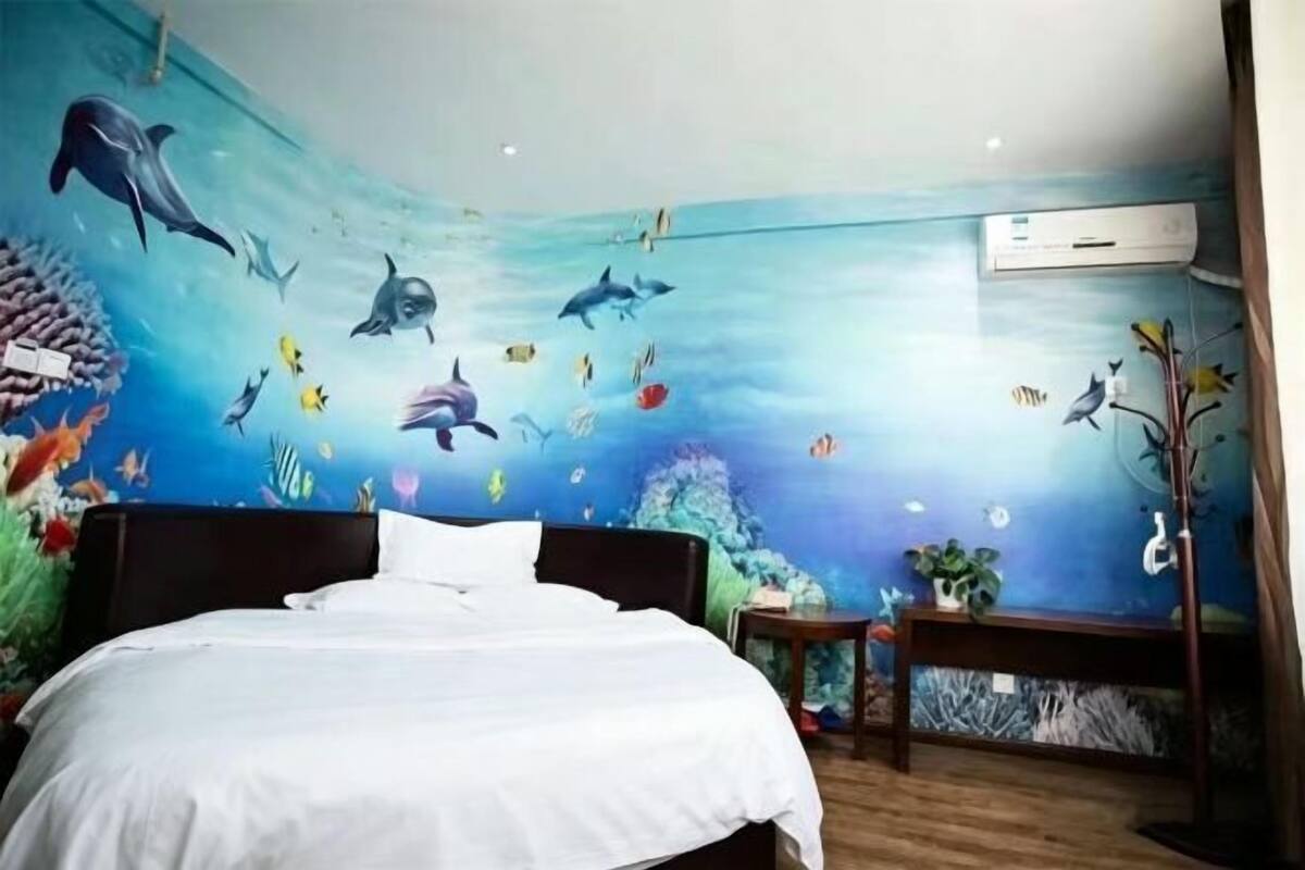 Ein Schlafzimmer mit Wandgemälde einer Unterwasserwelt, einem Bett, einem Nachttisch und einer Wand-Klimaanlage.