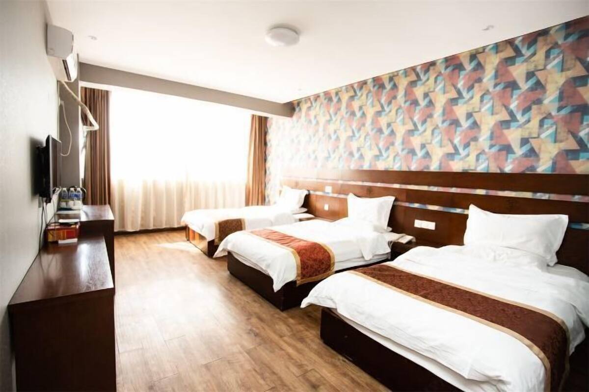 Ein Hotelzimmer mit drei Betten, einem Schreibtisch und einem Fernseher.