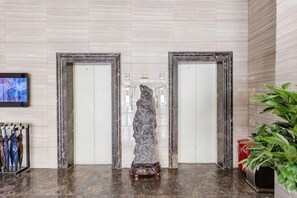 En lobby med to elevatorer, en skulptur, et fjernsyn og en plante.