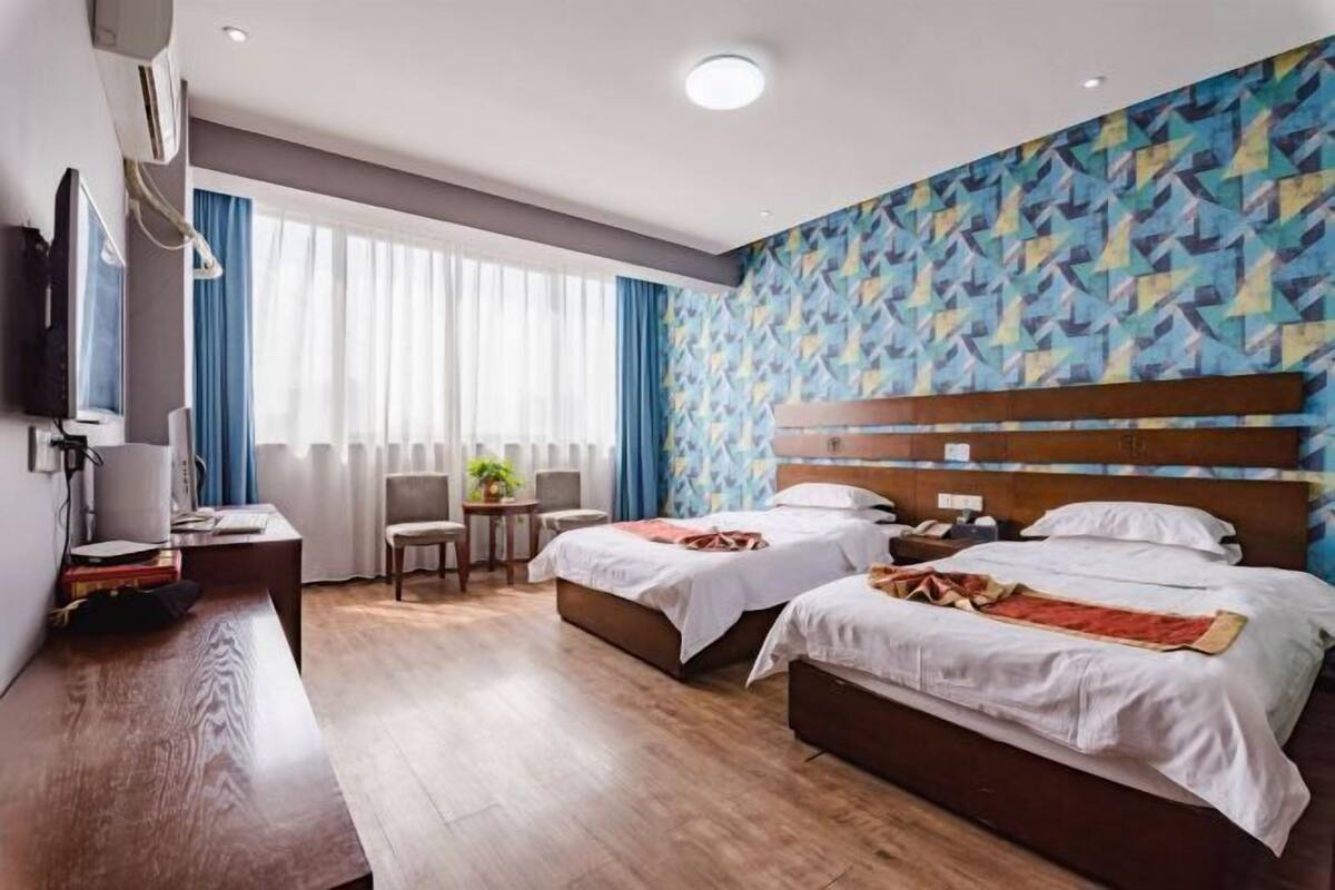 Ein Hotelzimmer mit zwei Betten, einem Schreibtisch, einem Stuhl, einem Fernseher und einem Fenster mit Vorhängen.