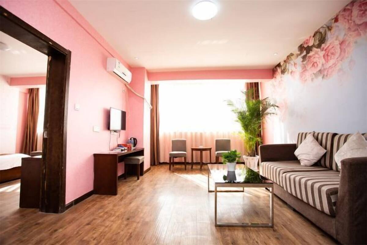 Ein Zimmer mit Holzboden, einer Couch, einem Fernseher, einem Schreibtisch und einer Topfpflanze.