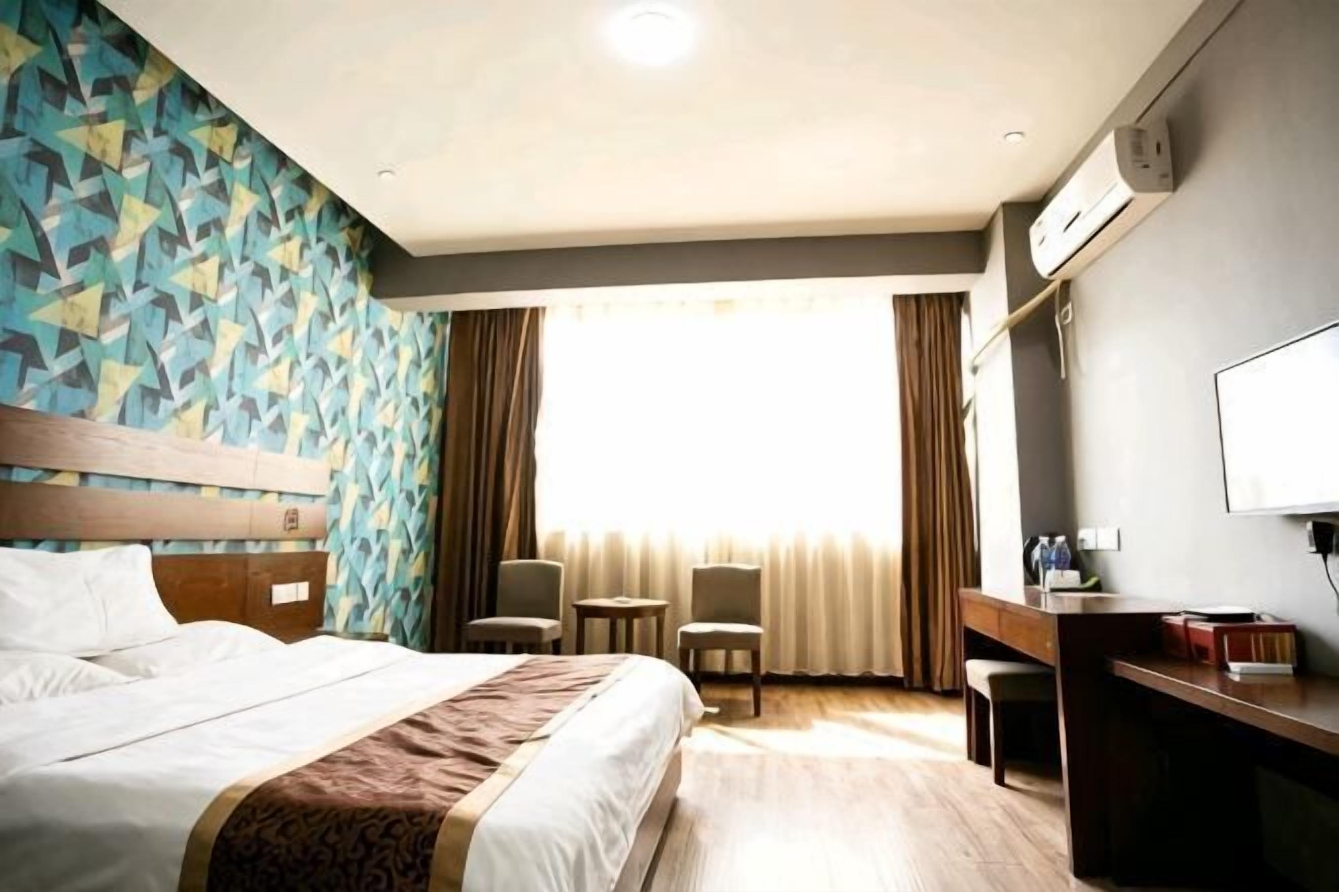 Ein Hotelzimmer mit Bett, Schreibtisch, Stuhl, Fernseher und einem fensterbepflanzten Fenster.