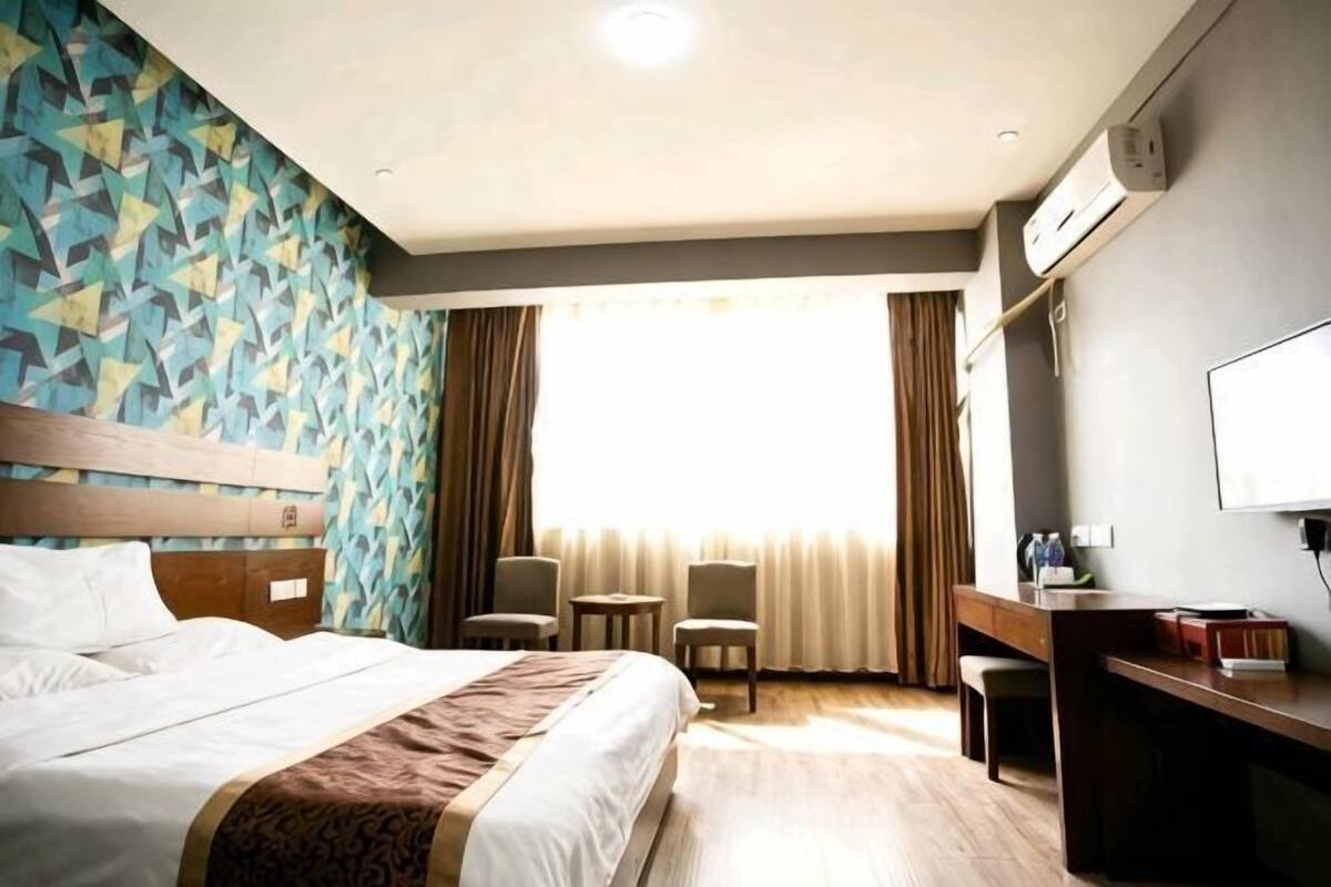 Ein Hotelzimmer mit Bett, Schreibtisch, Stuhl, Fernseher und einem fensterbepflanzten Fenster.