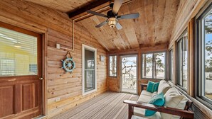 A wooden cabin interior with a ceiling fan, a wooden bench, a sofa with cushions, and large windows offering a view of the outdoors. - Port Peninsula Waterfront Paradise - Waterfront with Dock & Boat Lift (Oriental)