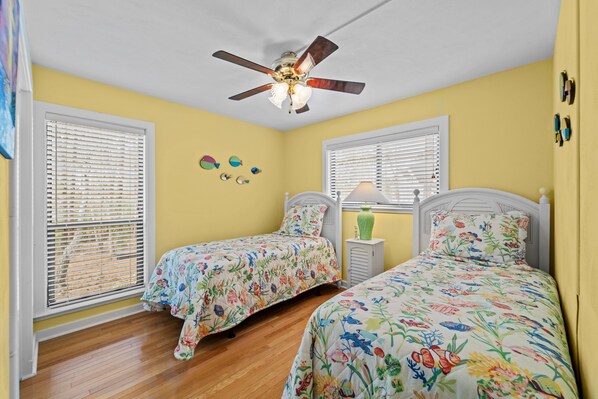A bedroom with two beds, a ceiling fan, and a window with blinds.