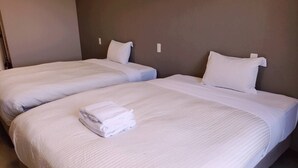 A hotel room with two single beds, each with white linens and pillows, and a neatly folded towel on the bed in the foreground. - Mr.KINJO Happiness Resort 1 (Miyakojima)